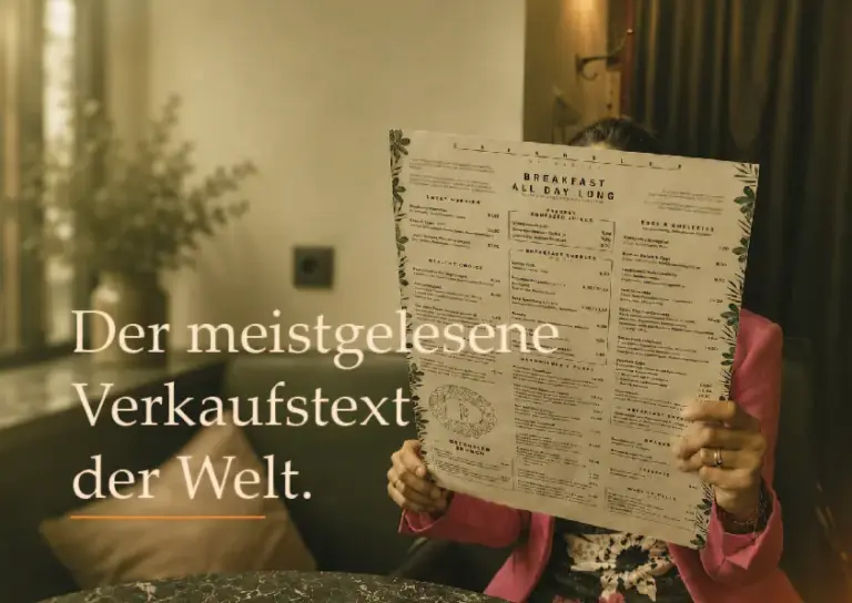 Person liest eine große Speisekarte im Café. Aufschrift: „Der meistgelesene Verkaufstext der Welt.“