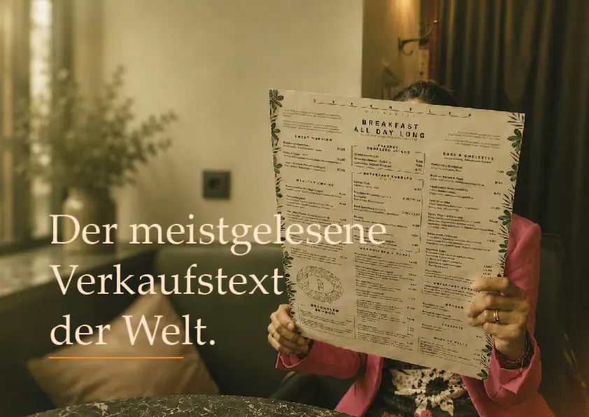 Person liest eine große Speisekarte im Café. Aufschrift: „Der meistgelesene Verkaufstext der Welt.“